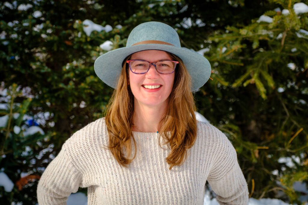 Woman wearing a wool blue hat with brown hair in front of trees.